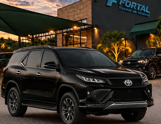 Toyota SW4 preta estacionada diante de uma fachada com o logo Fortal, ao entardecer